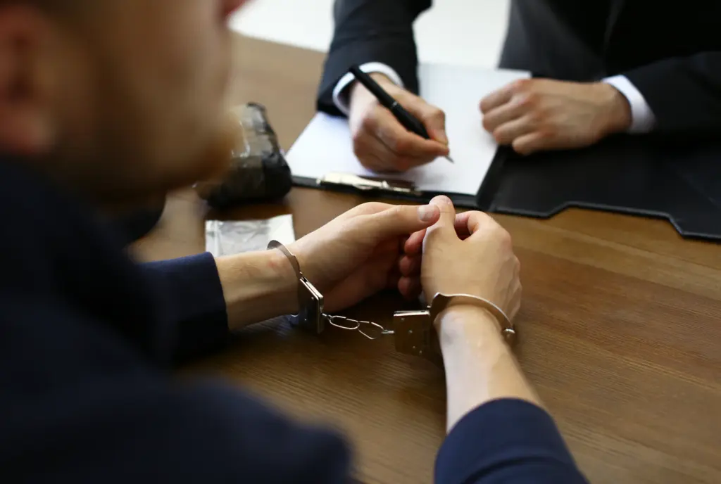 A person in handcuffs across the table from a lawyer